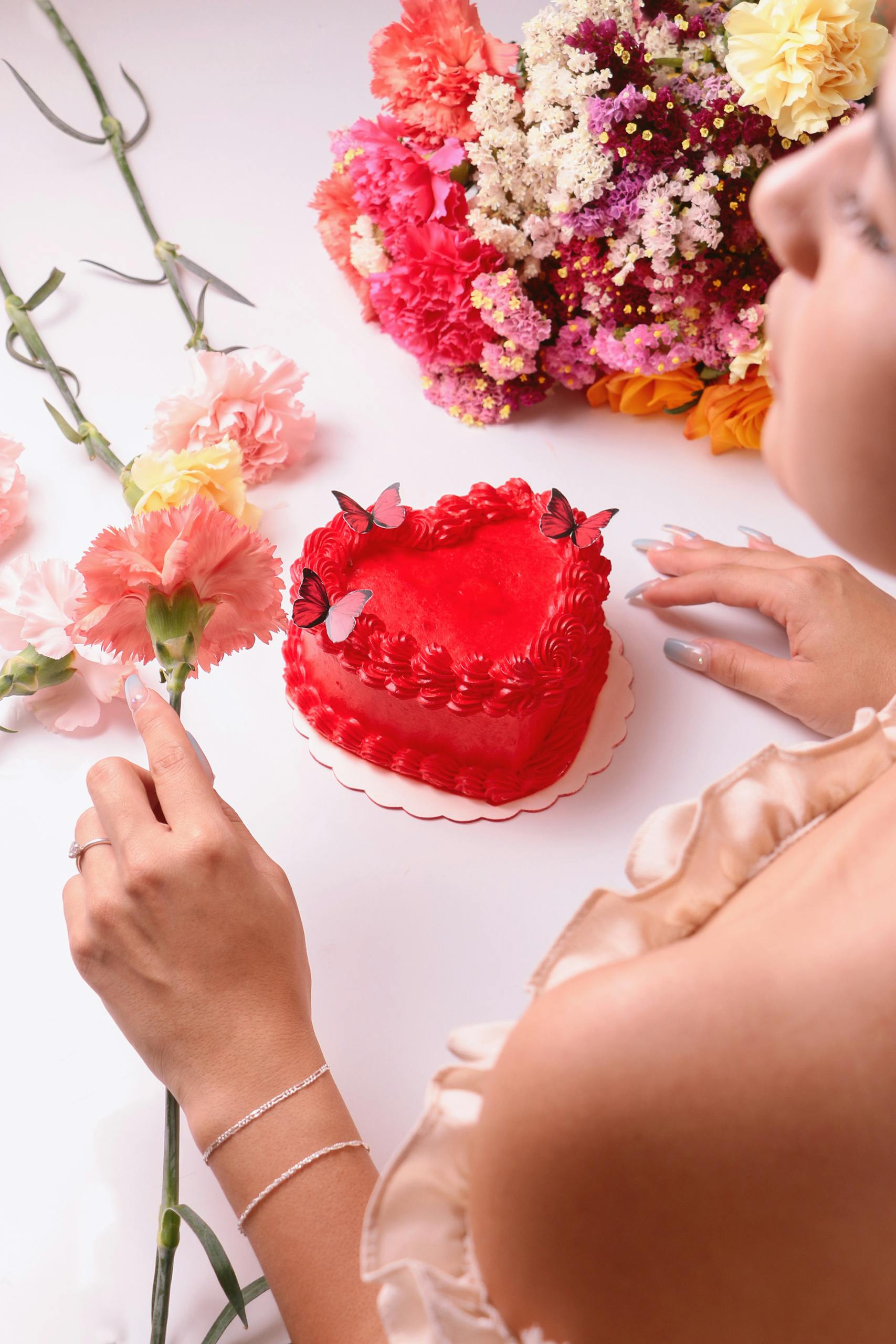 A heart-shaped red cake surrounded by vibrant flowers, capturing romance and sweetness.